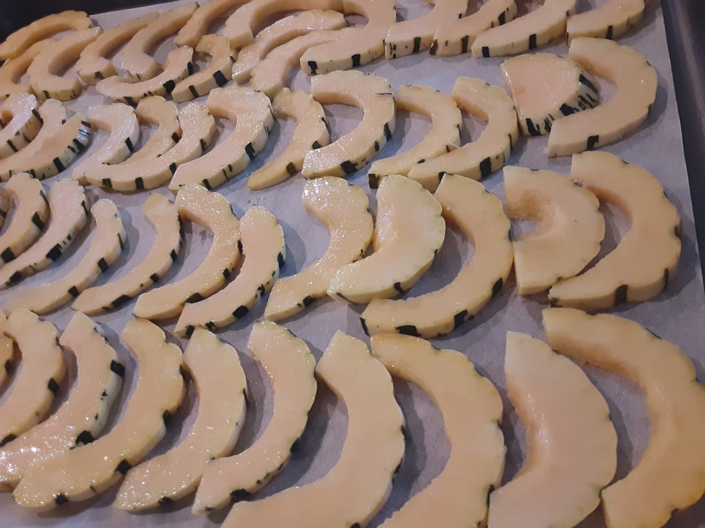 Delicata squash and sweet dumpling squash slices, tossed in oil, on a pan ready for baking.